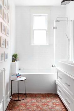 a white bathroom with a rug on the floor and pictures on the wall above it