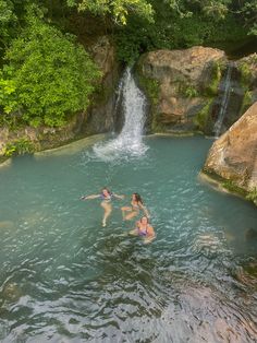 two people are swimming in the water near a waterfall