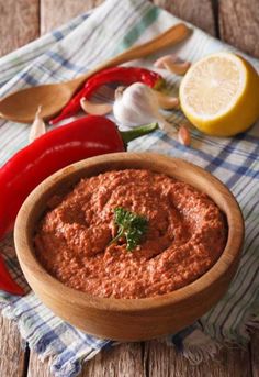 a wooden bowl filled with red sauce next to sliced peppers and lemons on a table