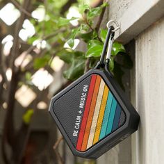 a multicolored speaker hanging from the side of a wall next to a tree