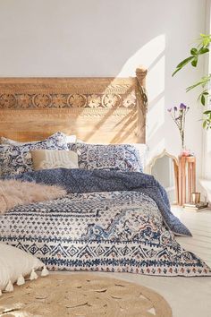 a bed with blue and white comforter in a room next to a plant on the floor