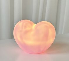 a pink heart shaped light sitting on top of a white table next to a curtain