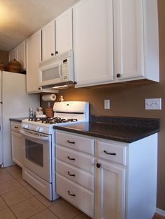 a kitchen with white cabinets and black counter tops, including a stove top oven next to a refrigerator