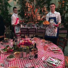 two men in aprons standing next to a table with plates and utensils