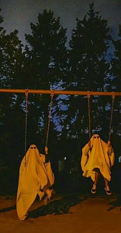 two people on swings covered in yellow cloths at night with trees in the background