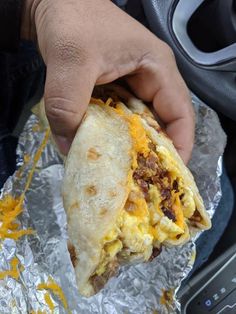 a person holding a burrito in their hand over foil covered with cheese and other toppings