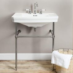 a white sink sitting on top of a wooden floor next to a basket filled with towels