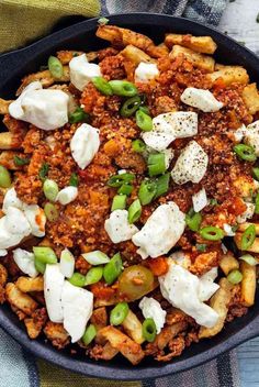 a skillet filled with pasta and cheese on top of a blue table cloth next to a wooden spoon