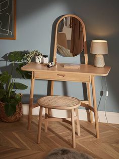 a wooden desk with a mirror, stool and lamp on it next to a potted plant