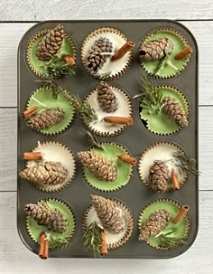 cupcakes decorated with pine cones, cinnamon sticks and green icing on a tray