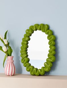 a vase with flowers and a mirror on a shelf