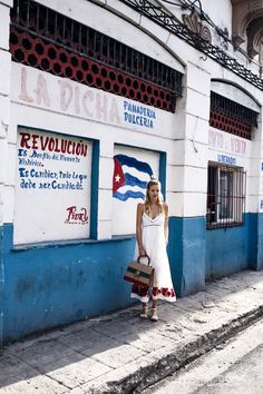 a woman in a white dress standing on the side of a building holding a suitcase