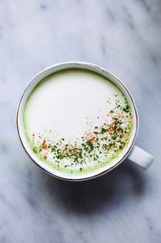 a cup filled with green liquid on top of a white countertop and topped with sprinkles