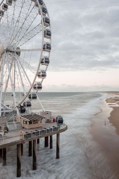 a ferris wheel sitting on top of a wooden pier next to the ocean under cloudy skies