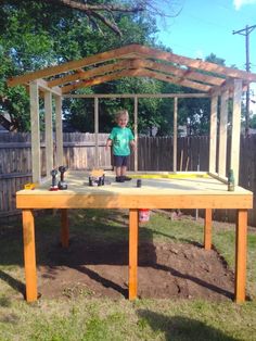 a little boy standing on top of a wooden table in the yard with an umbrella over it