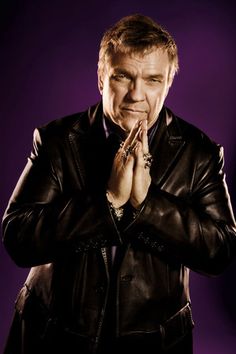 a man in a leather jacket is praying with his hands folded over his chest and looking at the camera