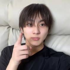 a young man sitting on top of a white couch holding his finger up to the camera