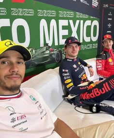 three men sitting on top of white couches in front of a green and red sign