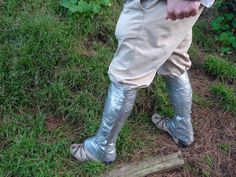 a man in silver boots standing next to a wooden stick on the ground with grass and bushes behind him