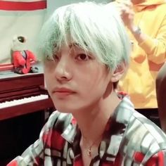 a man with green hair sitting in front of a piano and another person standing behind him