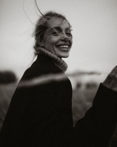 a black and white photo of a woman with her hair blowing in the wind smiling