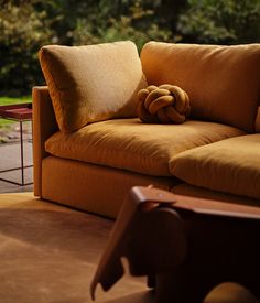 a brown couch with two pillows on it's back and some trees in the background