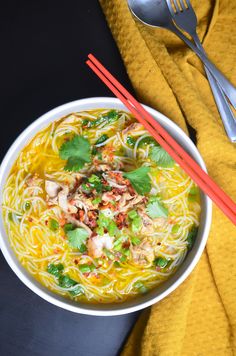 a white bowl filled with noodle soup next to two red chopsticks and a yellow towel