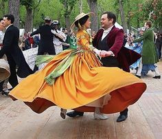 two people dressed in period costumes dancing on a wooden floor with other people around them