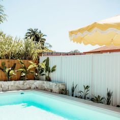 an empty swimming pool next to a wooden fence and umbrellas in the back yard