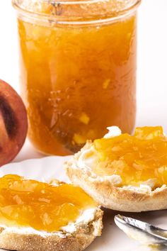 two pieces of bread sitting on top of a white plate next to a jar of peach jam