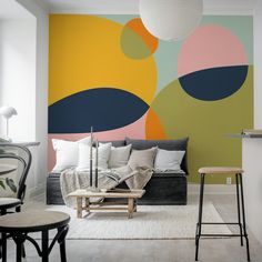 a living room with a couch, chair and table in front of a colorful wall