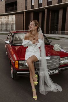 a bride sitting on the hood of a red car