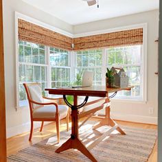 a room with a table, chair and laptop on the desk in front of two windows