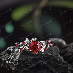 a red stone ring sitting on top of a rock with leaves and vines around it