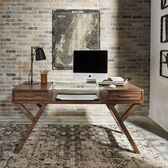 a desk with a computer on top of it in front of a brick wall and rug