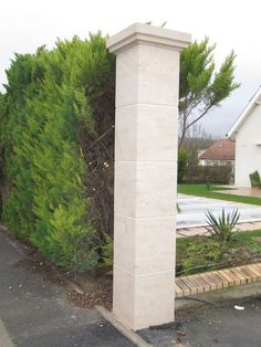 a tall white pillar sitting next to a lush green tree covered park area in front of a house