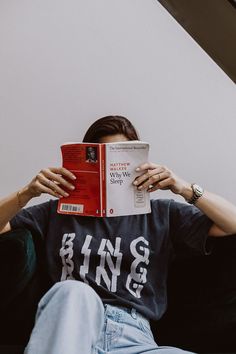 a person sitting down reading a book with their hands on their head and eyes closed