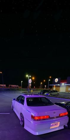 two white cars parked in a parking lot at night with the lights on and stars above them