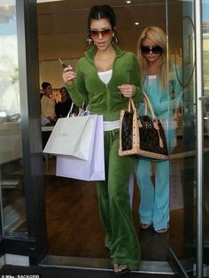 two women walking out of a glass door holding shopping bags and cell phones in their hands