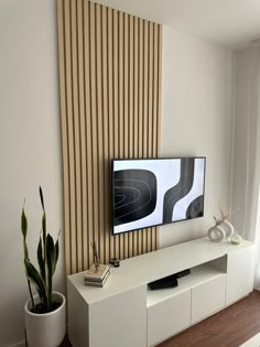 a flat screen tv sitting on top of a white entertainment center next to a potted plant