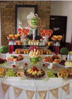 a table topped with lots of different types of fruit and desserts next to a brick wall