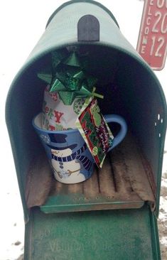 a green mailbox with a blue and white mug on it's side, wrapped in christmas presents