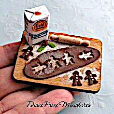 a hand holding a small wooden tray with cookies and milk on it next to a carton of biscuits