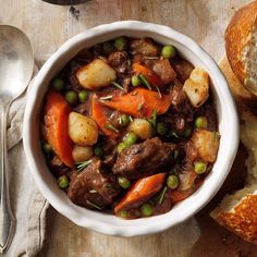 a white bowl filled with meat and vegetables next to a piece of bread on top of a cutting board