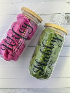 two jars filled with green and pink candy wrappers on top of a white wooden table