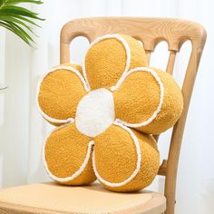 a yellow flower pillow sitting on top of a wooden chair next to a potted plant