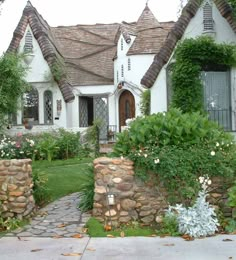 a white house with lots of plants and flowers around it