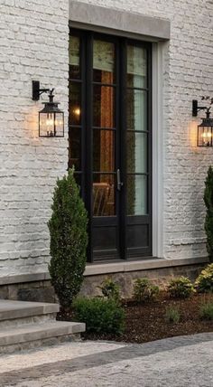 a white brick building with two black doors and some lights on the side of it