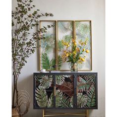 two paintings on the wall above a cabinet with flowers and plants in vases next to it