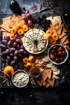 an assortment of cheeses, crackers and grapes on a platter with spider web decoration